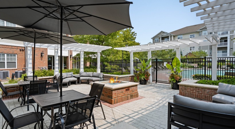 Outdoor courtyard firepit with shaded pergola, lounge seating, and pathway to pool