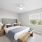 Model bedroom at our apartments for rent in Dedham, MA, featuring windows with blinds and carpeted flooring.
