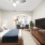 Staged bedroom with a bed, entertainment cabinet, tv, and seperate seating area featuring two blue chairs and an end table.