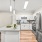 Staged kitchen at our apartments for rent  in Dedham, featuring stainless steel appliances, white cabinetry, natural wood grain plank flooring, and quartz counters with a kitchen island.