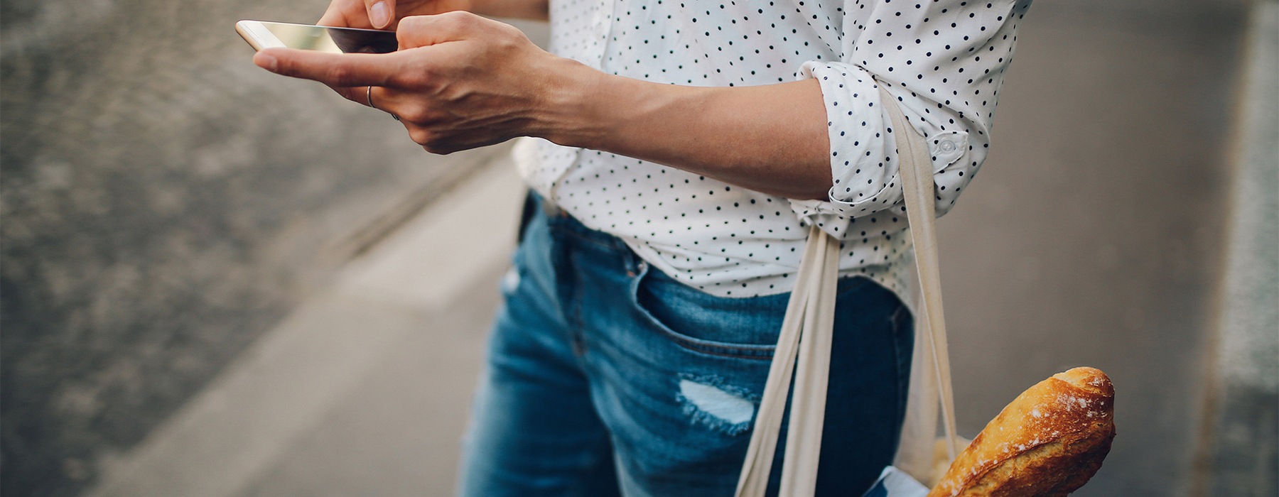 Woman on her phone while holding a bag with bread